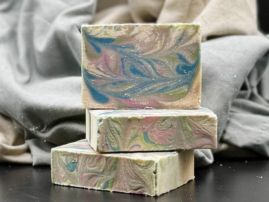 Three marbled soap bars stacked on a dark surface with a gray fabric background
