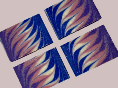 Four square soap bars with purple, pink, white, and blue swirl patterns on a light pink background/.