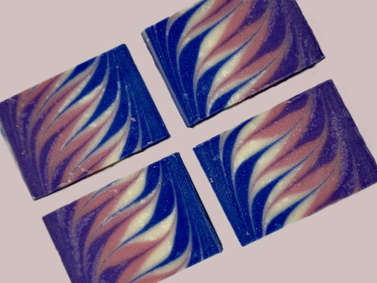 Four square soap bars with purple, pink, white, and blue swirl patterns on a light pink background/.