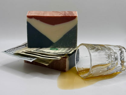 Bar of red, white, and blue soap with money and a glass of alcohol on a gray background