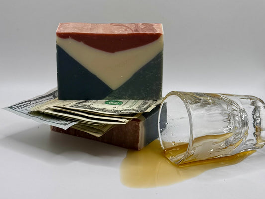 Bar of red, white, and blue soap with money and a glass of alcohol on a gray background