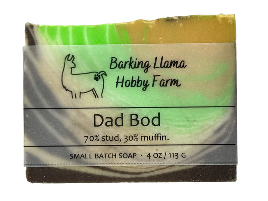 An orange, green, white, and brown bar of soap with the Barking Llama Hobby Farm label and logo. The title of the soap is "Dad Bod" with the tagline "70 percent stud, 30 percent muffin."