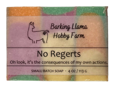 A rectangular bar of handmade soap wrapped in a paper label from Barking Llama Hobby Farm, featuring a multicolor pastel design with a line drawing of a llama and the text 'No Regrets'.