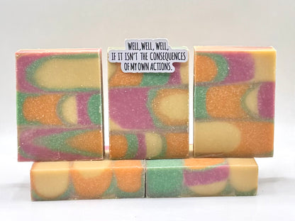 Five handmade rectangular bars of soap with a marbled swirl pattern of orange, purple, green, and cream, arranged on a white background. The center bar has a small white paper label with black text that reads, 'WELL, WELL, WELL, IF IT ISN'T THE CONSEQUENCES OF MY OWN ACTIONS.